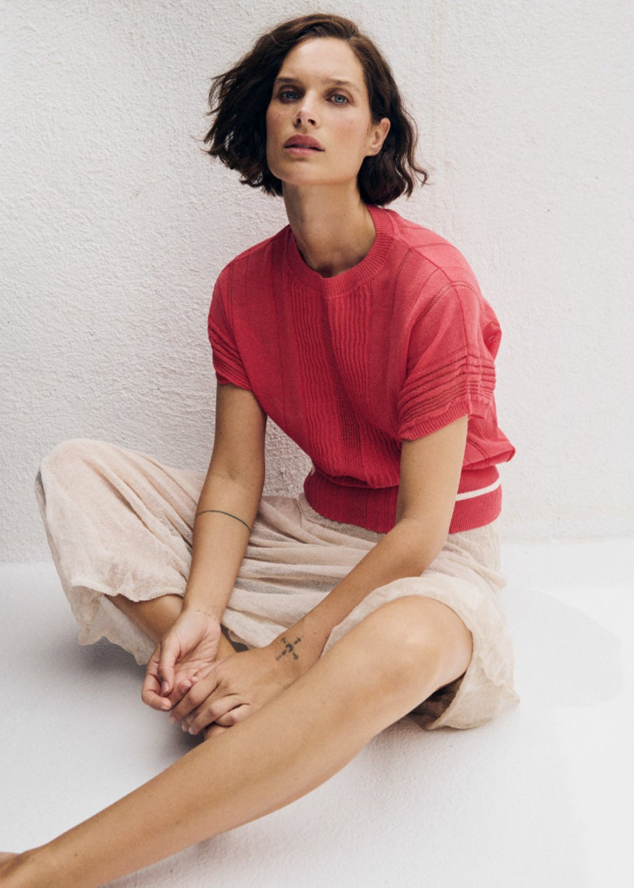Woman sitting on a white floor wearing a red sweater and beige pants, with text overlay.