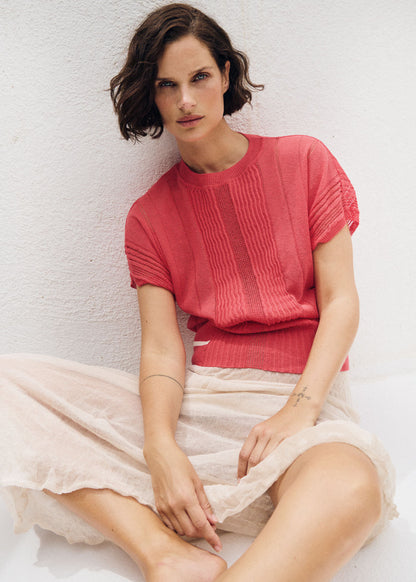 Woman wearing a pink top and light skirt against a white background