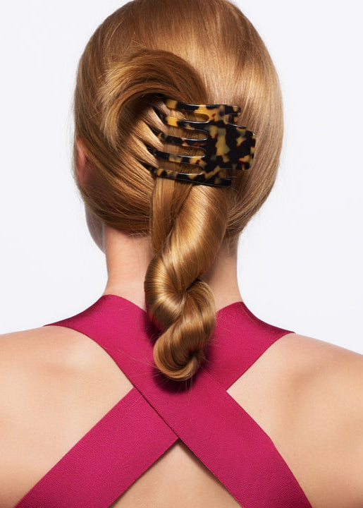 Person with a styled hair bun using a decorative hair clip on a plain background