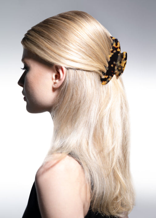 Woman with long blonde hair wearing a leopard print hair accessory on a plain background