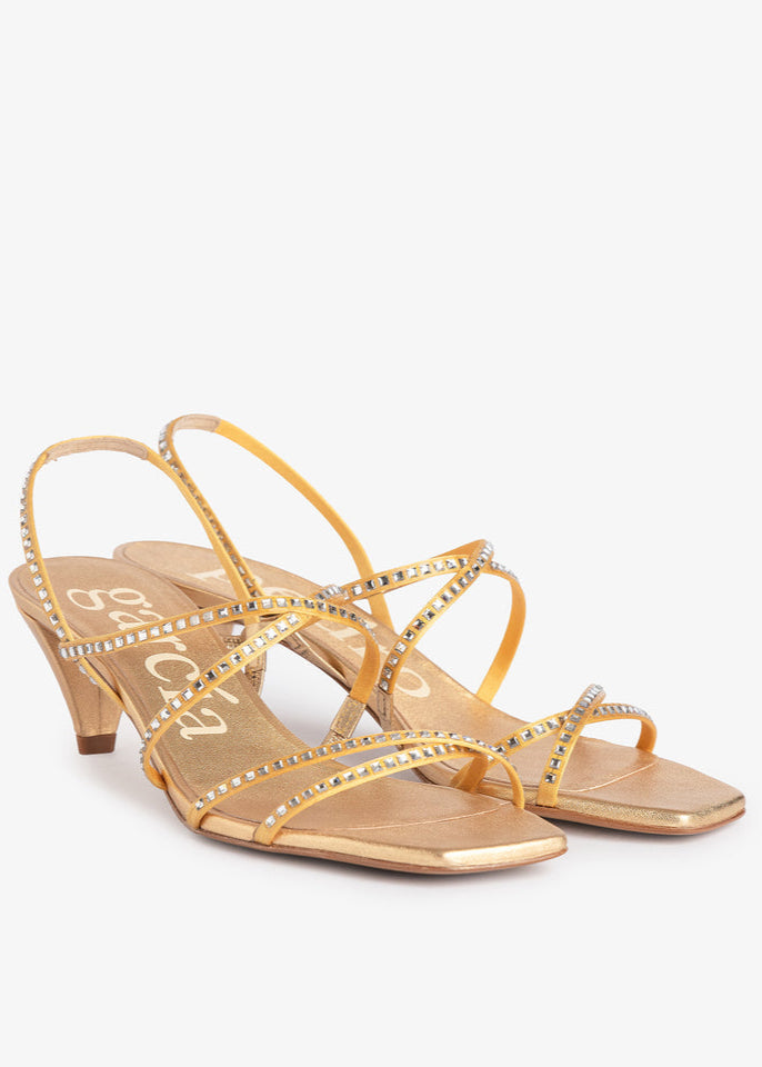 Gold high-heeled sandals with rhinestone details on a white background