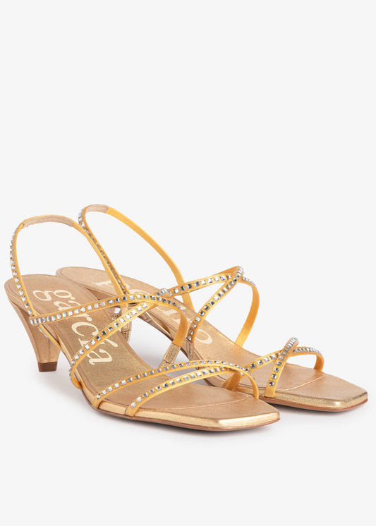 Gold high-heeled sandals with rhinestone details on a white background