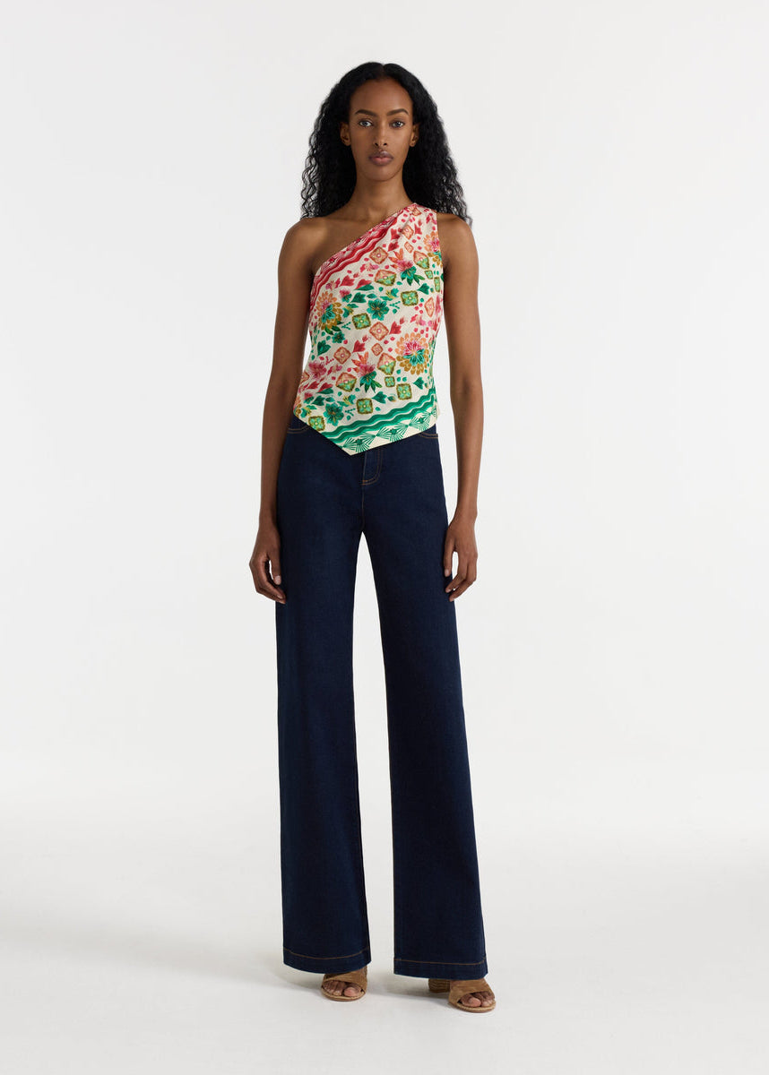 Woman wearing a floral one-shoulder top and dark blue jeans on a white background