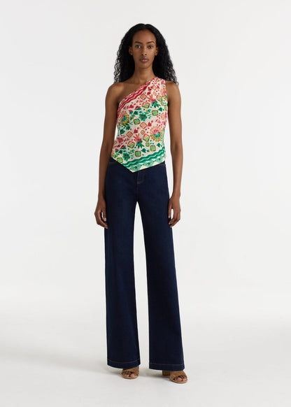 Woman wearing a floral one-shoulder top and dark blue jeans on a white background