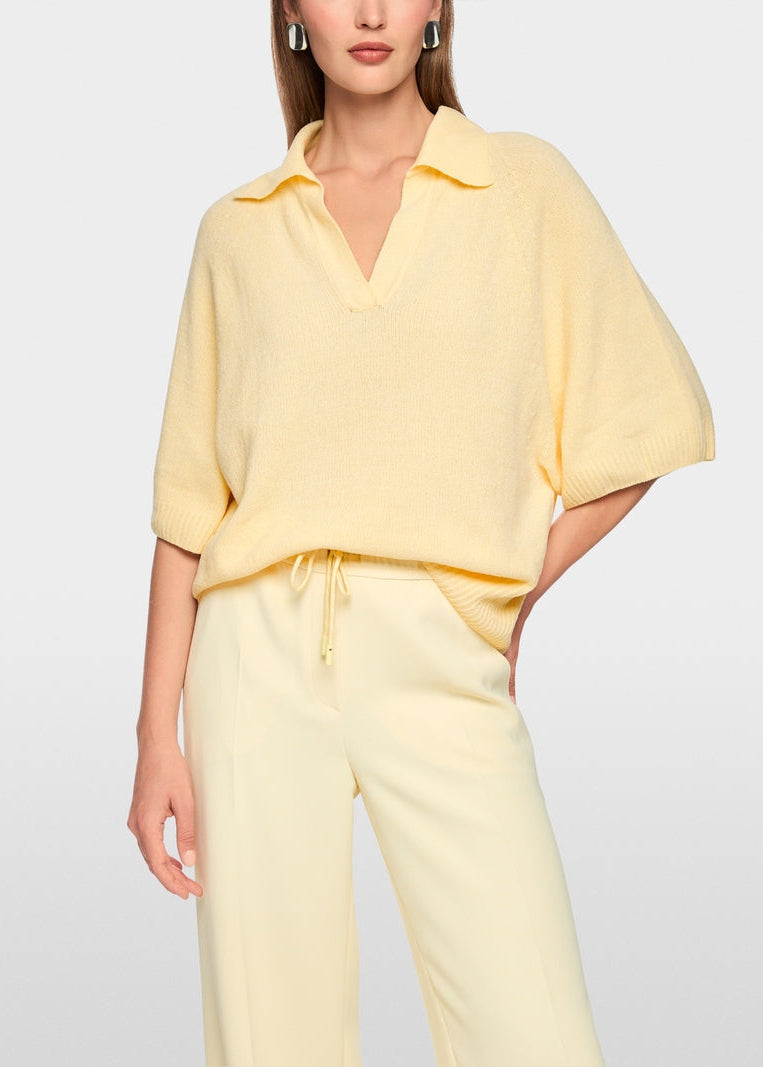 A woman wearing a pale yellow short-sleeve collared knit top and matching light yellow drawstring pants, photographed against a clean light gray studio background.