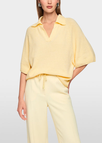 A woman wearing a pale yellow short-sleeve collared knit top and matching light yellow drawstring pants, photographed against a clean light gray studio background.