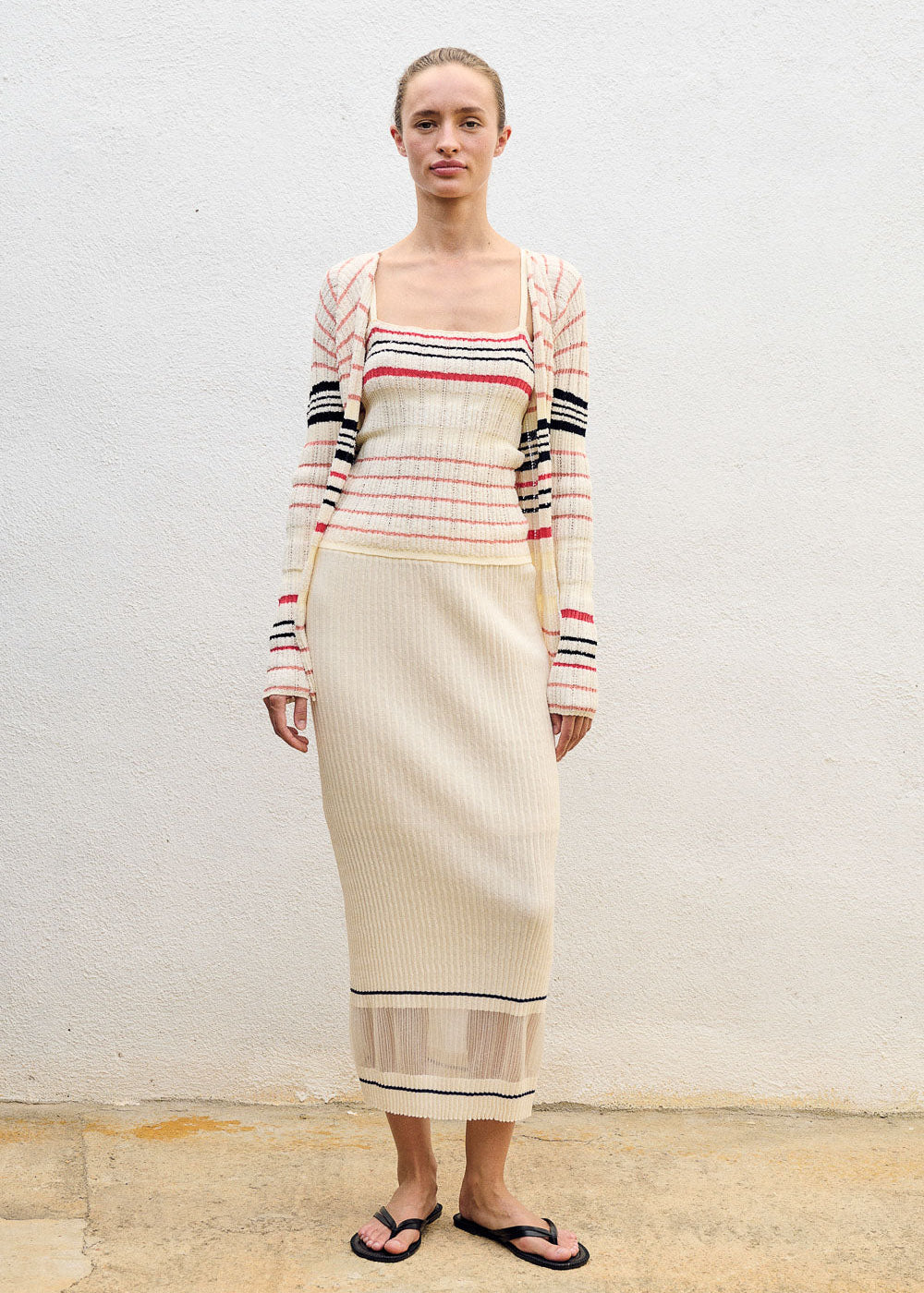 Woman wearing a long, cream-colored dress with a striped top against a plain background