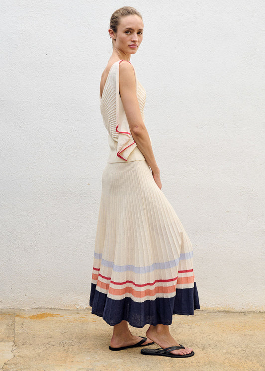 Woman wearing a long, cream-colored dress with colorful stripes on a plain background