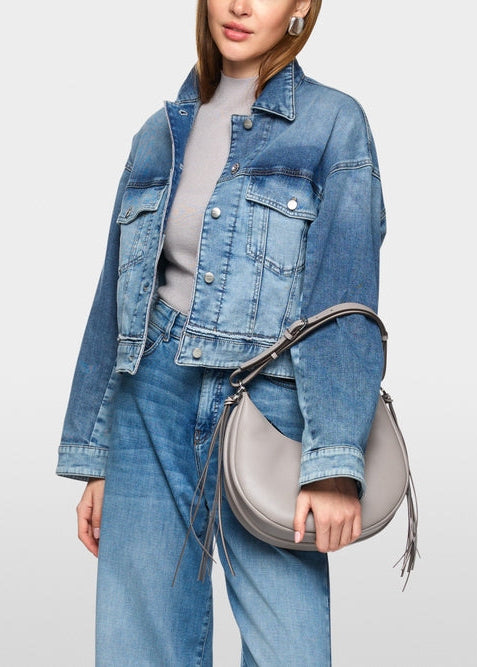 Person wearing a denim jacket and jeans holding a gray handbag on a light gray background