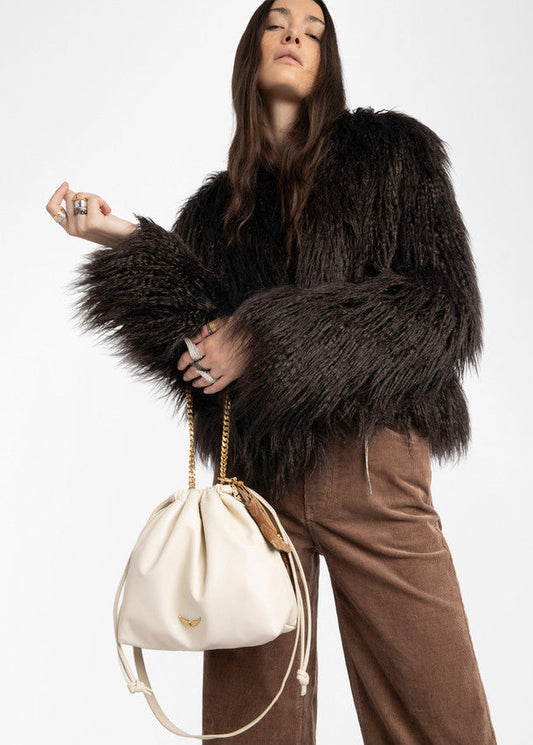 Person wearing a dark brown shaggy coat holding a white handbag on a light gray background