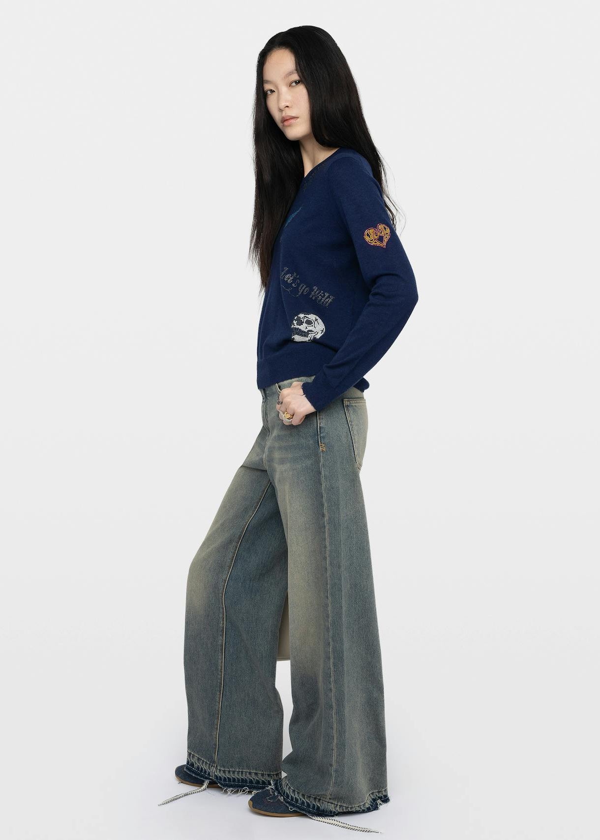 Woman wearing a navy sweater with text and graphics, paired with wide-leg jeans on a white background