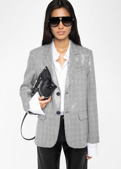 Person wearing a gray checkered blazer with a white shirt and black pants, holding a black handbag on a white background.