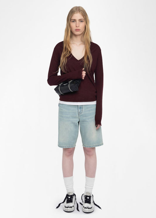 Woman wearing a maroon sweater, light blue shorts, and black sneakers on a white background