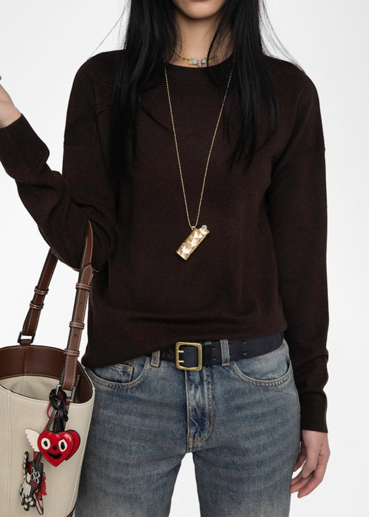 Person wearing a brown sweater and blue jeans, holding a beige handbag with red heart design.