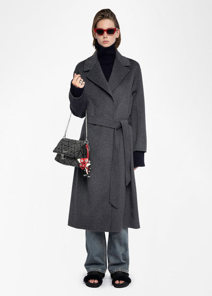 Person wearing a long gray coat holding a handbag on a white background